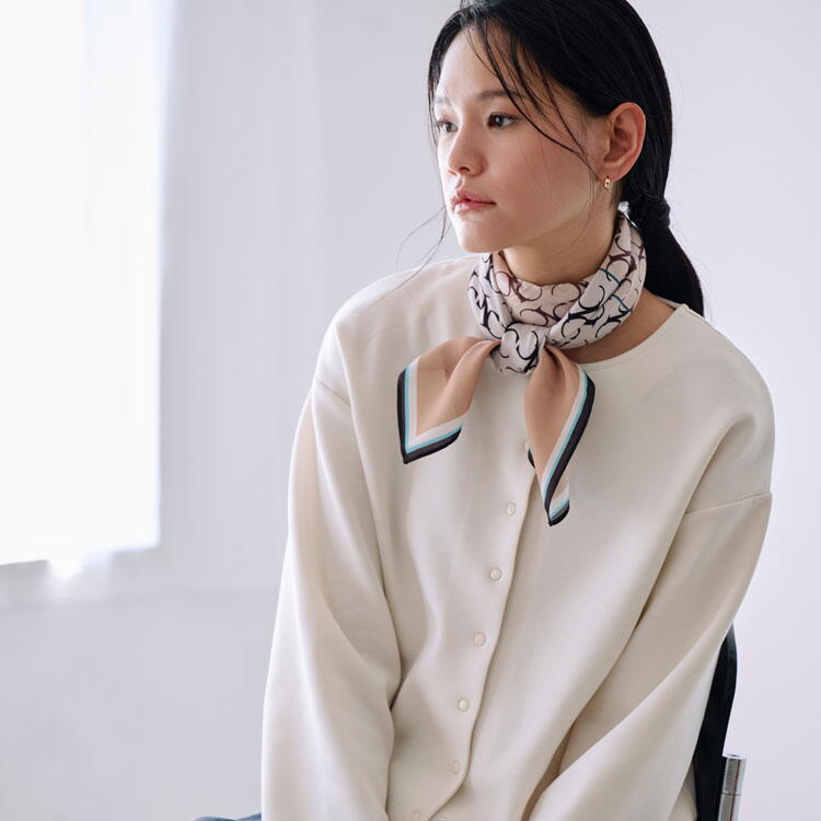 コムサイズム　白いシャツにベージュのカーディガンを羽織り、ベージュのスカートを履いた女性の写真