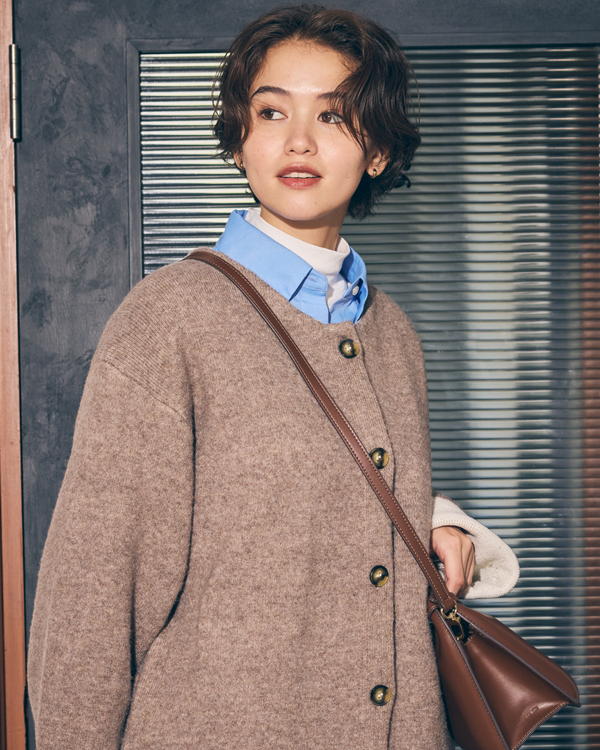 コムサイズム　白いカットソーに水色のシャツ、茶色のコーディガンを羽織り、グレーのズボンを履いた女性の写真