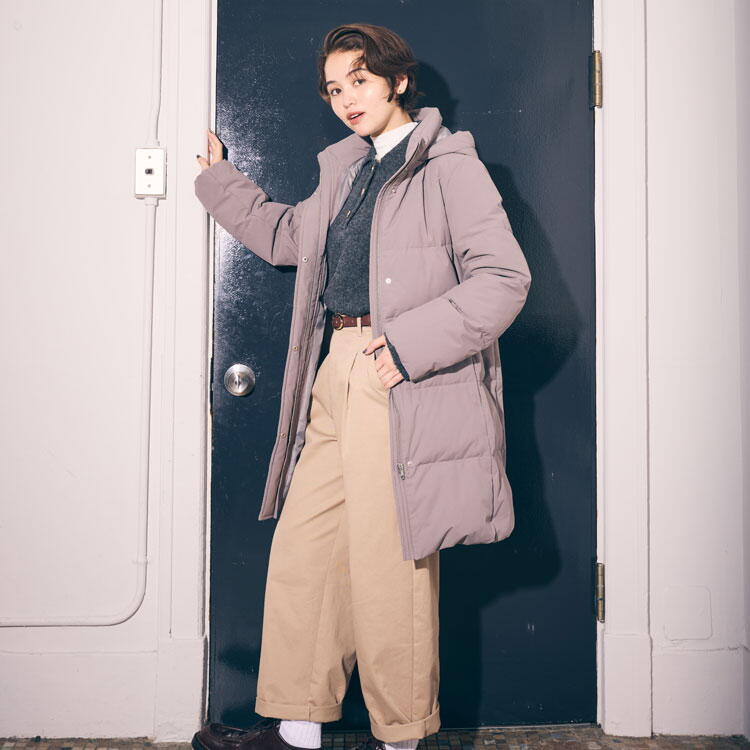 コムサイズム　白いシャツにグレーのニット、薄いピンクのダウンコートを羽織り、ベージュのズボンを履いた女性の写真